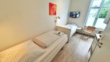 Ein Schlafzimmer mit einem Einzelbett, einem Schreibtisch, einem Stuhl, einem Fernseher und einem Fenster.