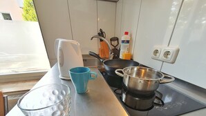 Una cocina con estufa, hervidor, taza azul, vaso y olla.