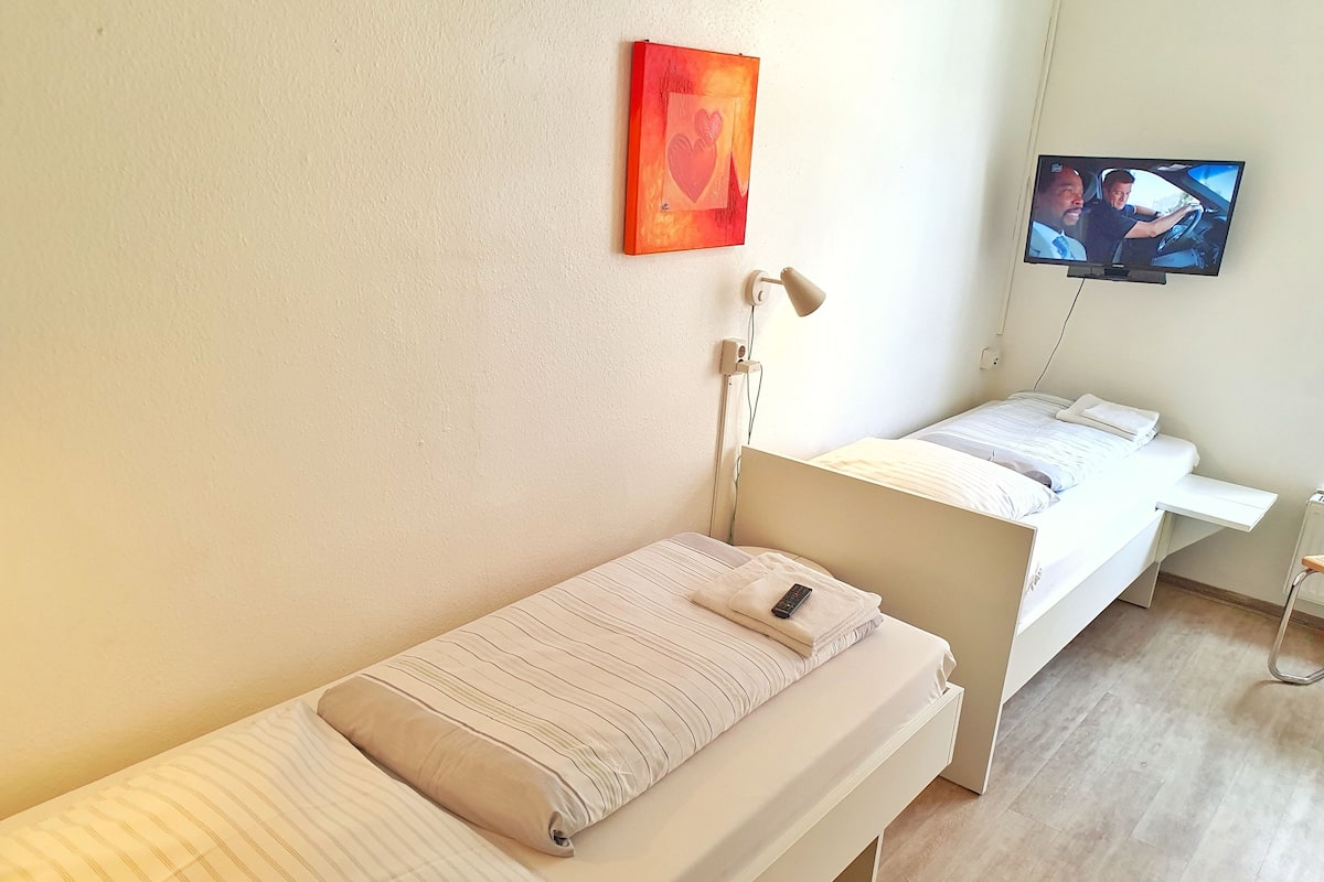 A single-bed room with a bedside table, a wall-mounted TV, and a painting.