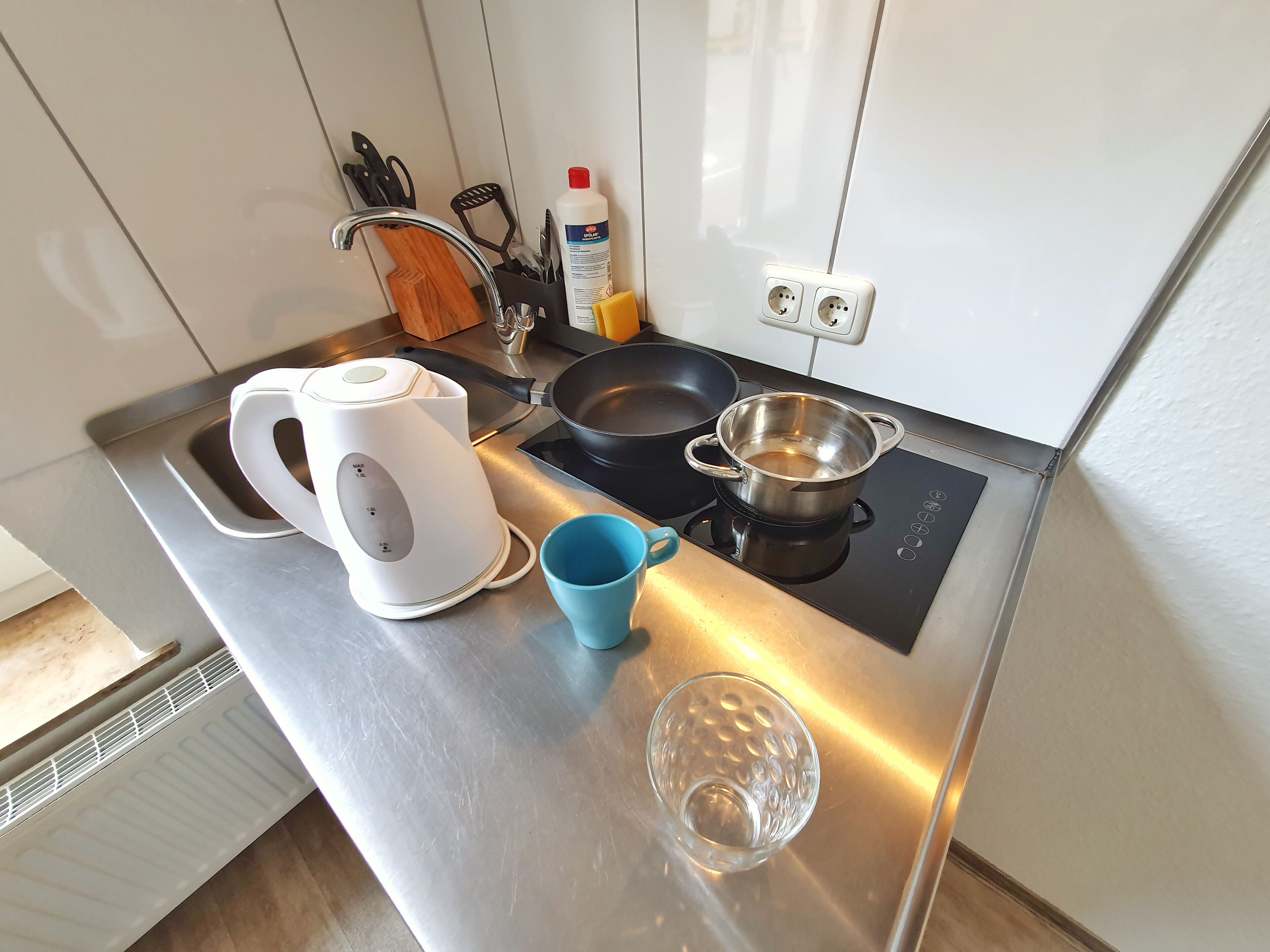 Una cocina moderna con una tetera, una sartén, una olla y una taza azul sobre la encimera.