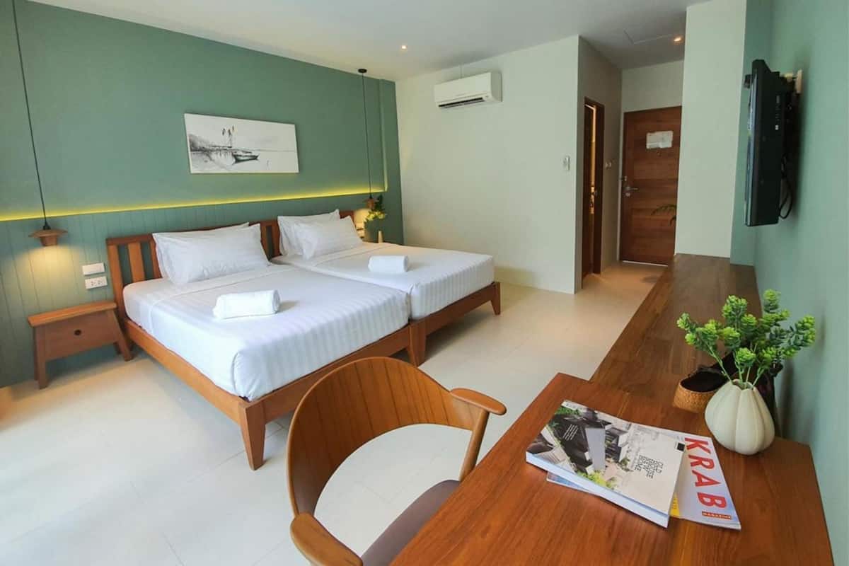 A hotel room with two beds, a wooden desk, a chair, a TV, and a plant.