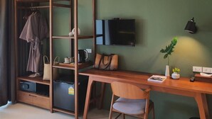 Une pièce de taille modeste, avec un bureau en bois, une chaise, un téléviseur fixé au mur, une armoire et une petite plante.