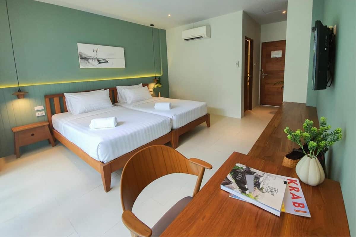 A hotel room with two beds, a wooden desk, a chair, a TV, and a potted plant.