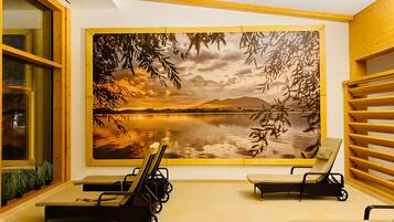 Una habitación con un gran mural en la pared que muestra un lago y montañas, dos sillones y una mesita.