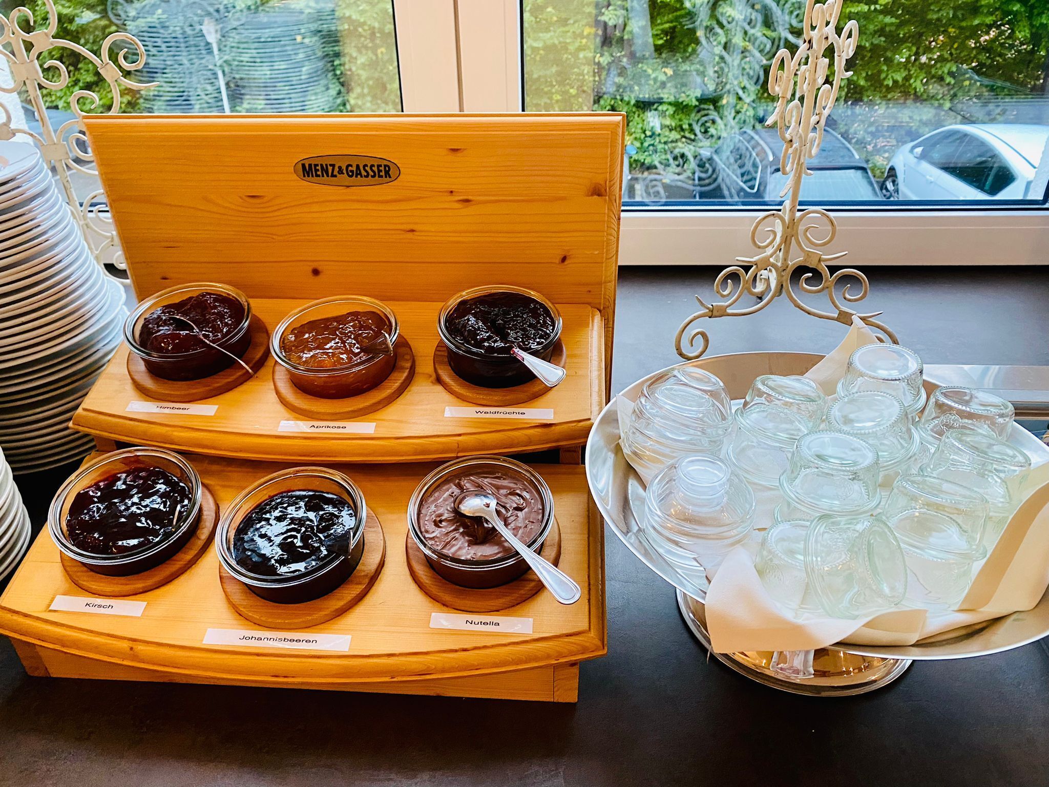A wooden display case with various types of spreads, including apricot, walnut, and chocolate, alongside a tray of empty glass jars.