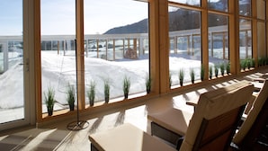 A sunlit room with large windows, wicker furniture, and potted plants. - Hotel Nesselwanger Hof (Nesselwang)