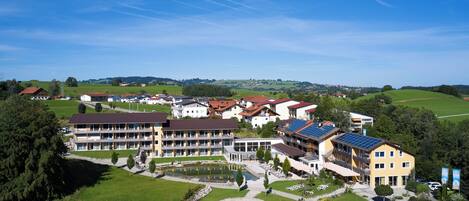 Un hotel de varios pisos con un patio central, rodeado de campos verdes y edificios residenciales.