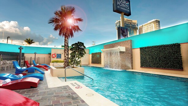 A pool area with lounge chairs, a palm tree, and a sign for 'Four Points by Sheraton'. - Four Points By Sheraton Queretaro Norte (Querétaro)