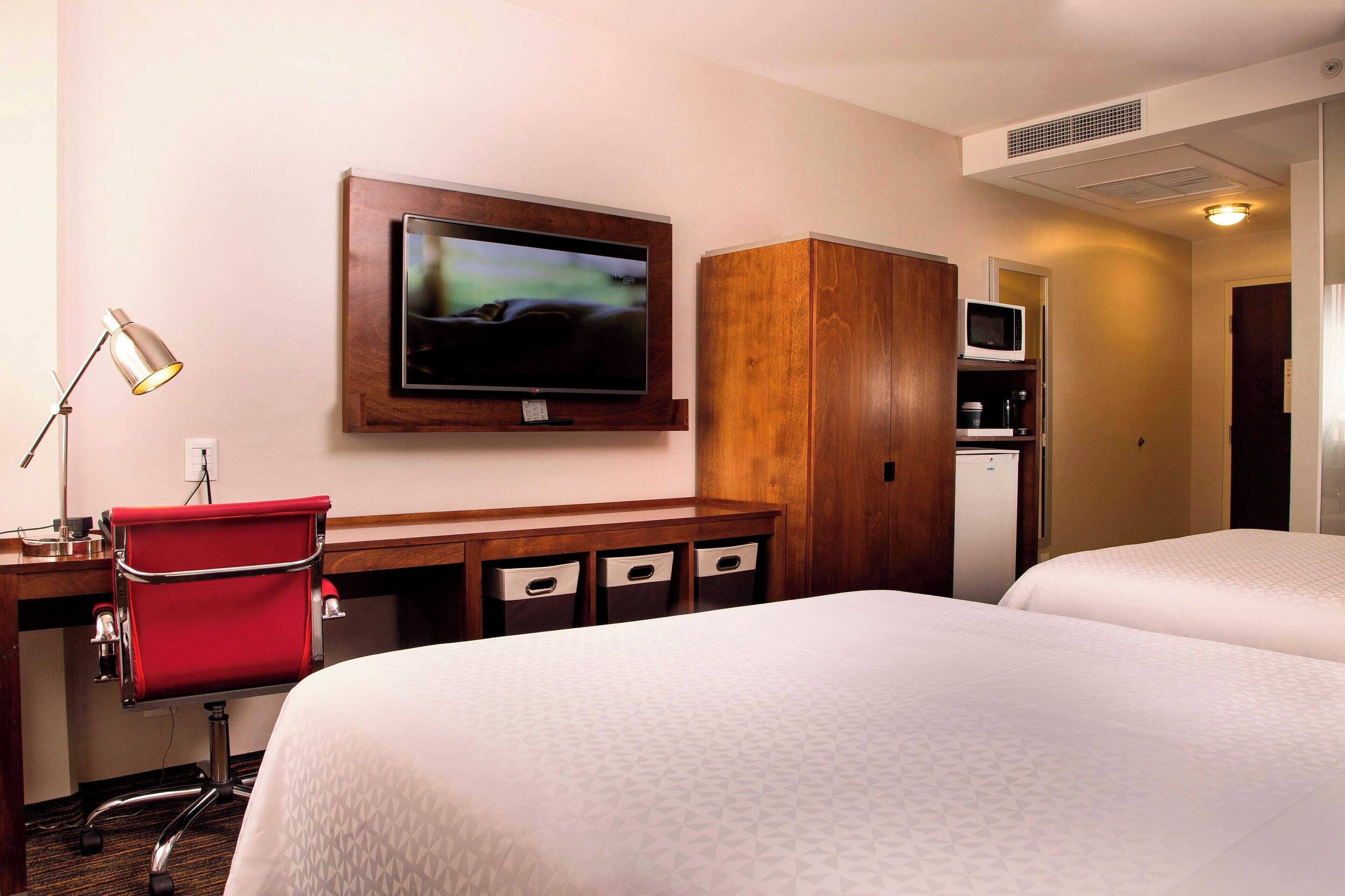 A hotel room with a bed, a desk with a chair, a television, a microwave, and a wardrobe.