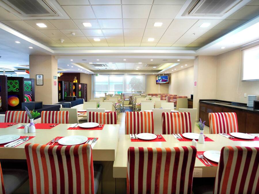 Un salón de conferencias con mesas dispuestas para comer, sillas y una pantalla de televisión en la pared.