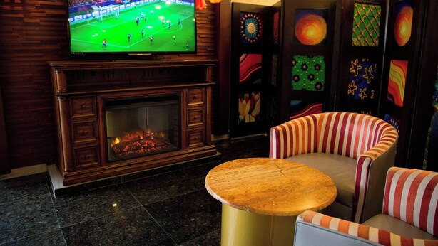 A room with a television displaying a soccer match, a fireplace, striped seating, and decorative panels. - Four Points By Sheraton Queretaro Norte (Querétaro)