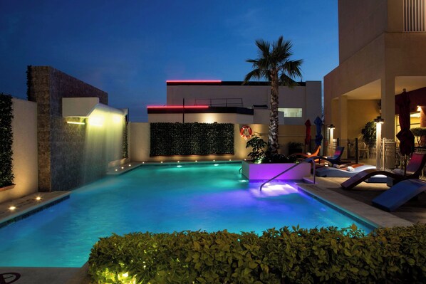 A swimming pool with a modern design, surrounded by a landscaped area with plants and a palm tree. - Four Points By Sheraton Queretaro Norte (Querétaro)