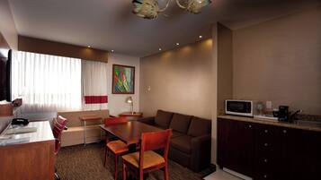 Habitación de hotel con mesa de comedor, sillas, sofá, televisor, microondas y pequeña cocina.