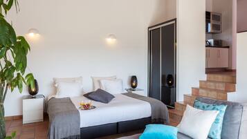 Quarto com cama, mesas de cabeceira, um criado-mudo, televisão, escada e área de cozinha.