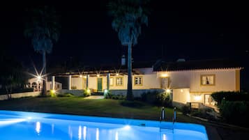 A nighttime view of a pool area with a house in the background.