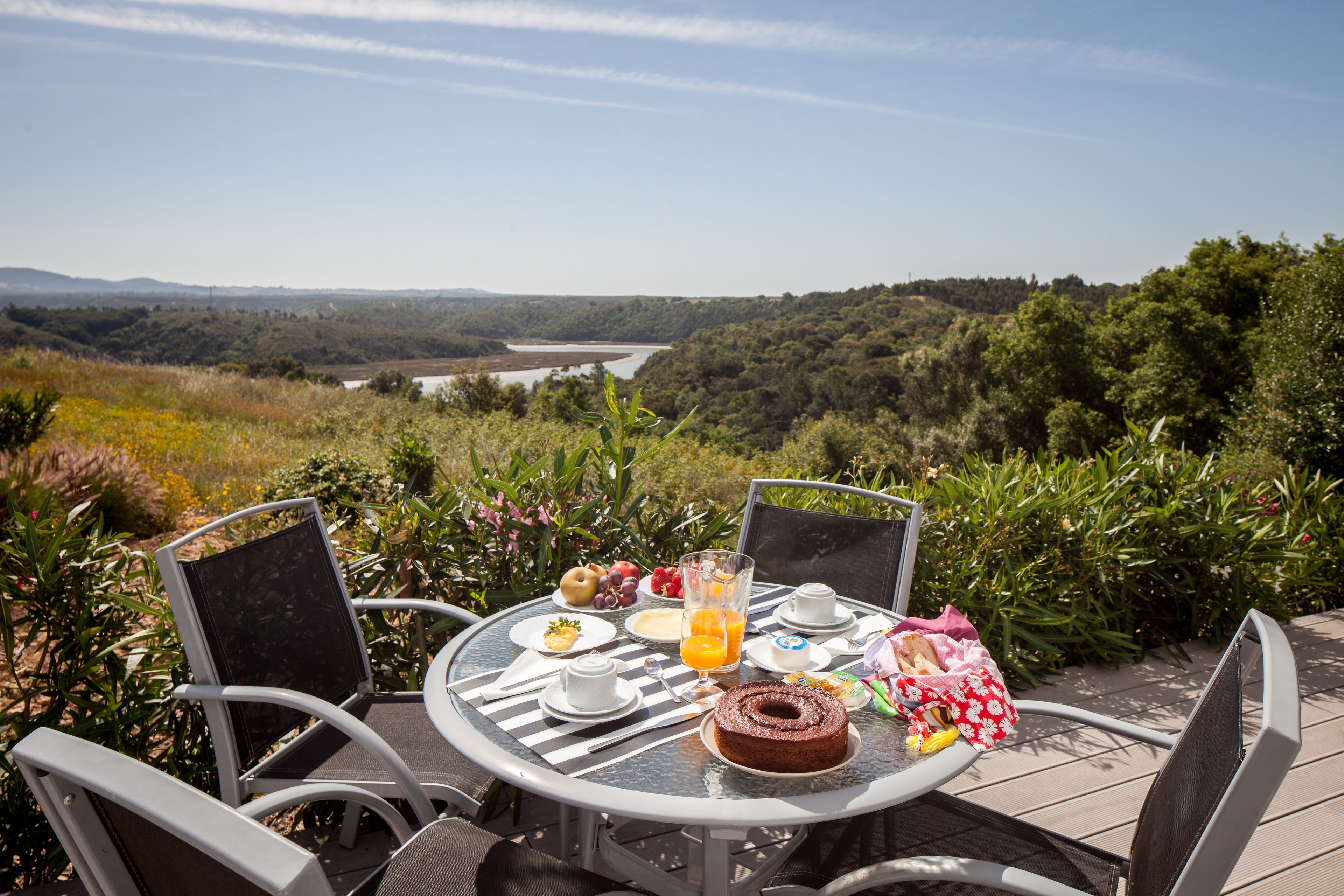 A round table with chairs set outdoors, overlooking a river and hills.