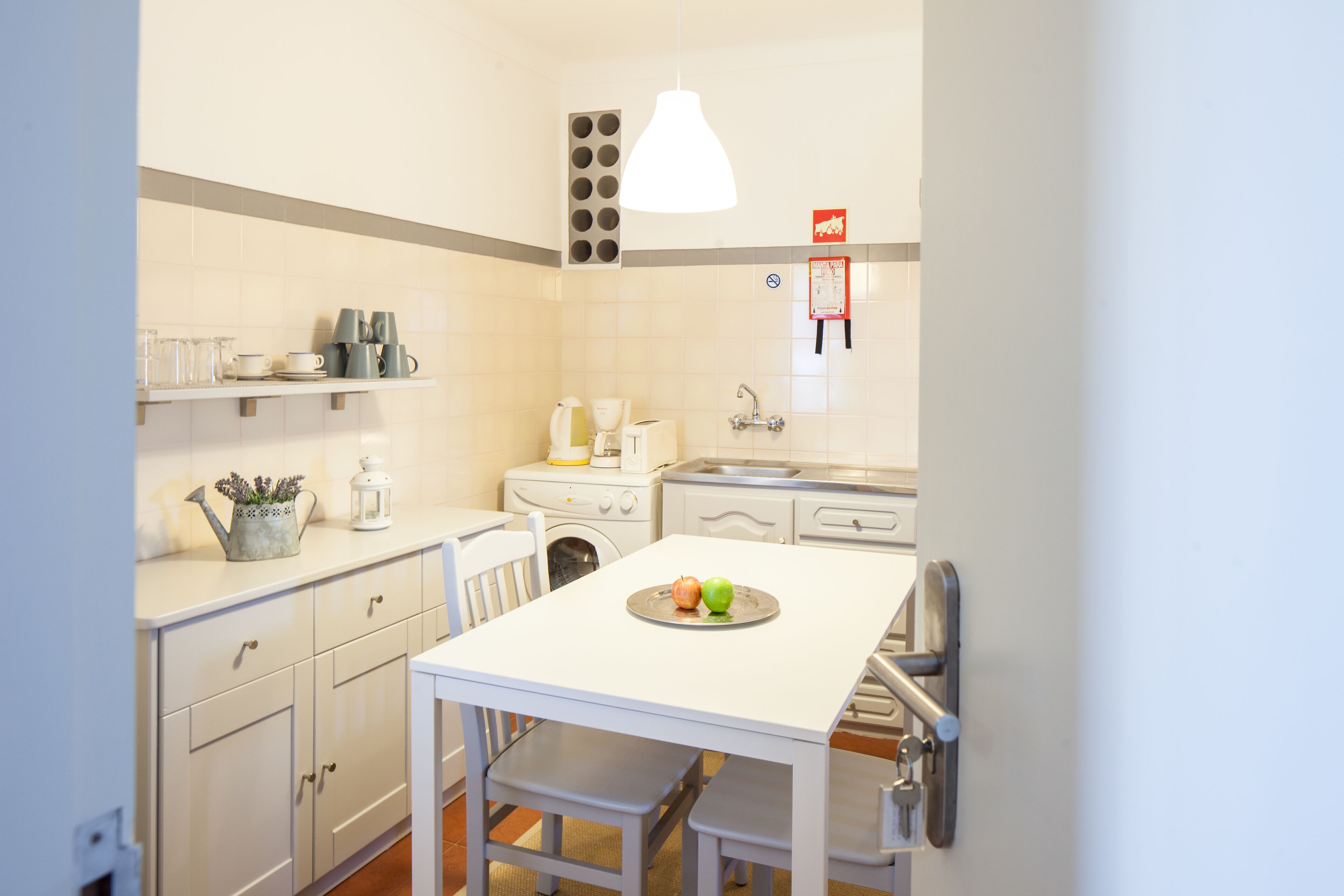 Una cucina compatta con pensili bianchi, un piccolo tavolo da pranzo e una lampada a sospensione.