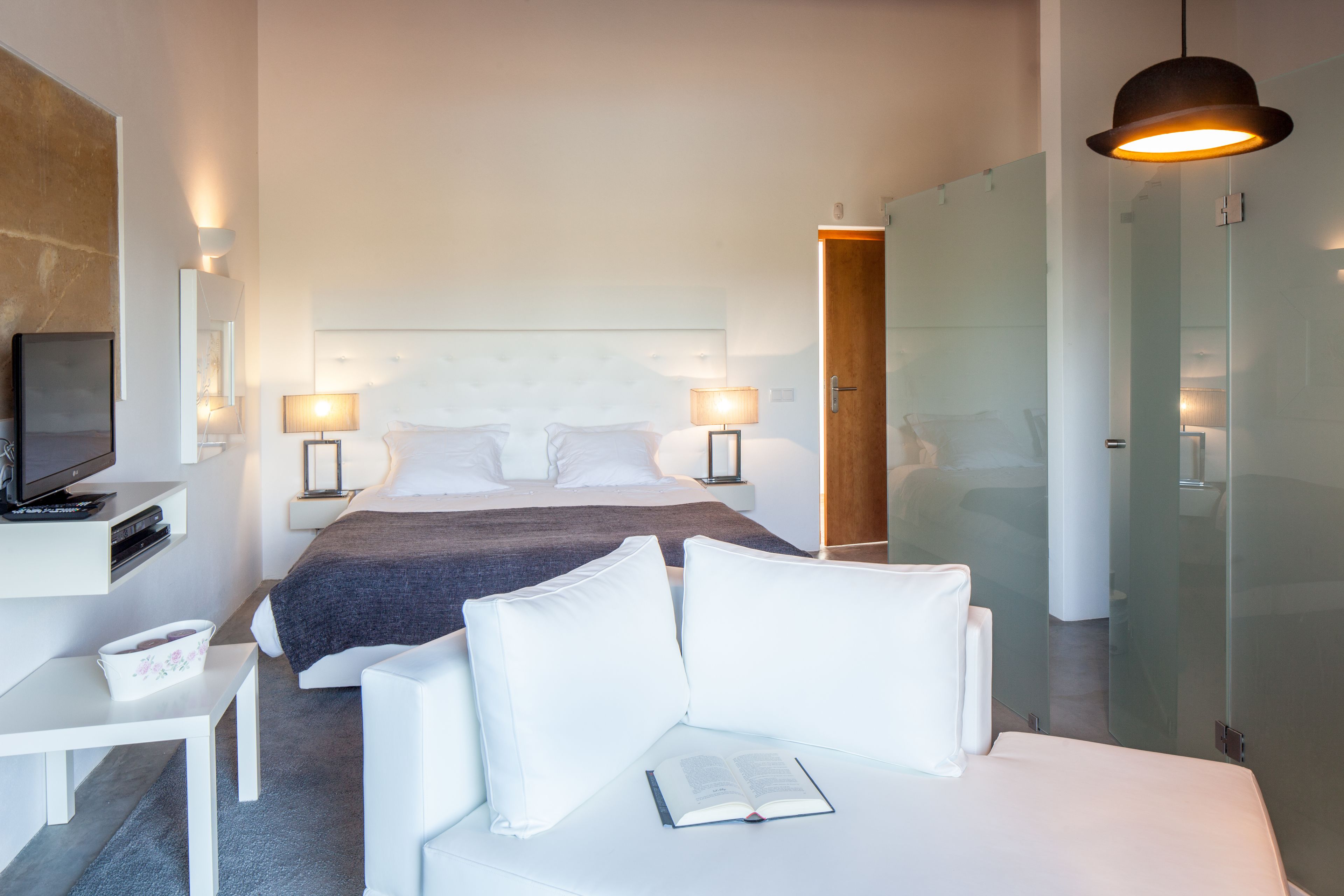 A modern hotel room with a bed, bedside lamps, a TV, a desk, and a reading area.