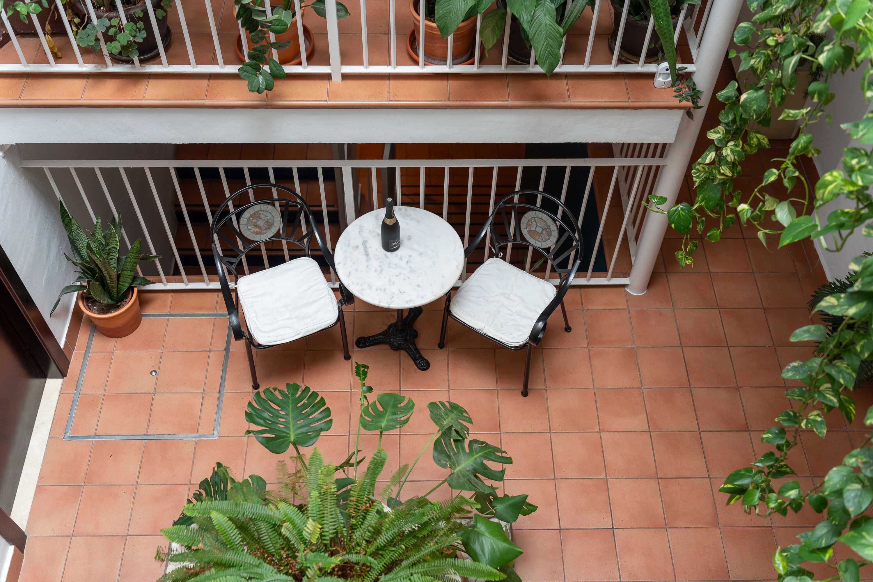 A balcony with two white cushioned chairs, a small round table, and a bottle of champagne.
