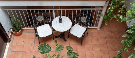 A balcony with two white cushioned chairs, a small round table, and a bottle of champagne.