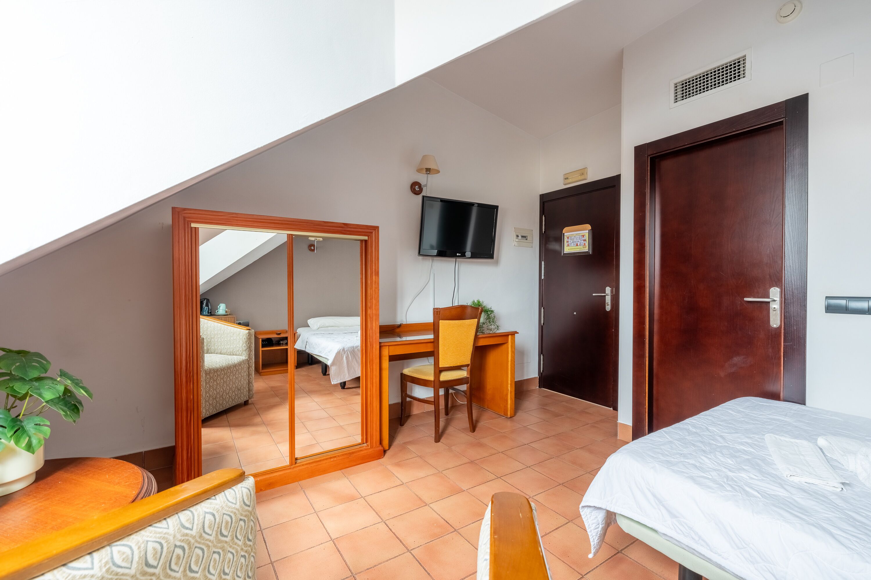 A room with a bed, a desk, a chair, a TV, and a mirror.