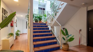 Una escalera con escalones azules que lleva a un rellano con plantas en macetas y una barandilla blanca.