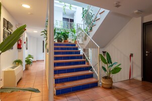 A staircase with blue steps leading to a landing area with potted plants and a white railing.
