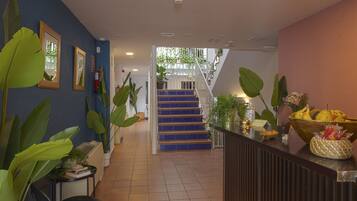 Un hall d’hôtel avec un escalier, des plantes en pot et un comptoir d’accueil agrémenté d’un panier de fruits.