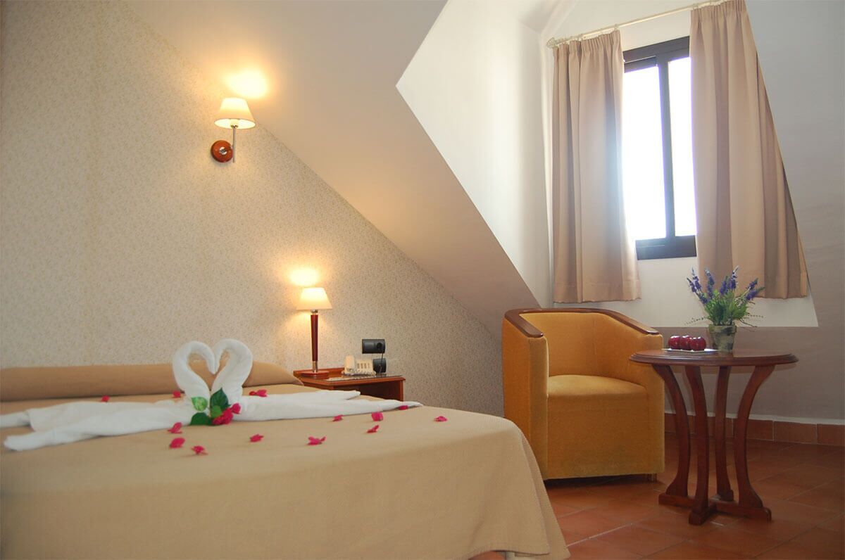 A hotel room with a bed, a chair, a small table, and a window with curtains.
