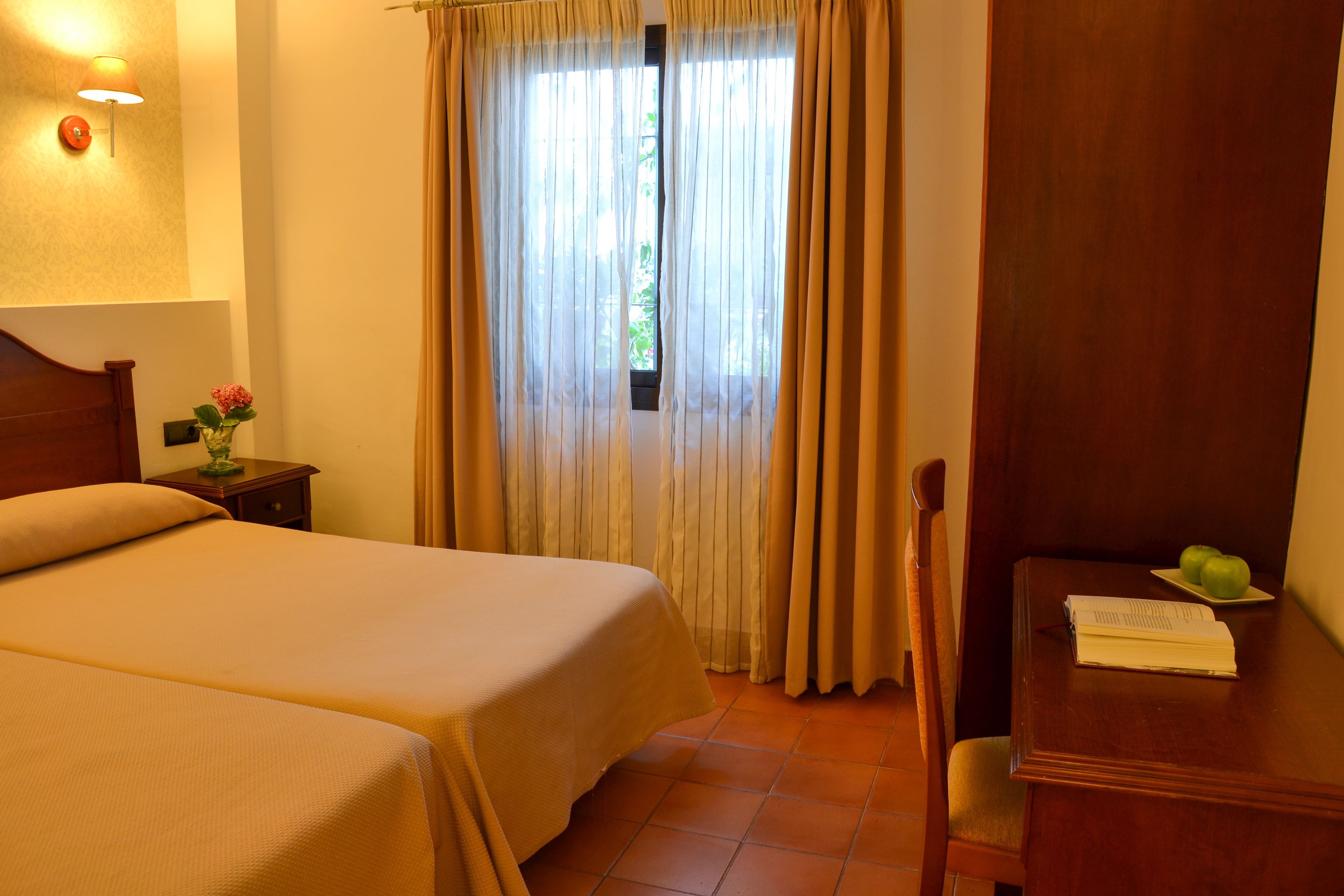 A hotel room with two beds, a desk with a chair, a lamp, and a window with curtains.