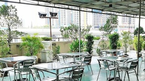 An outdoor cafe area with tables and chairs, surrounded by potted plants and a view of tall buildings in the background. - JB Central Hotel (Johor Bahru)