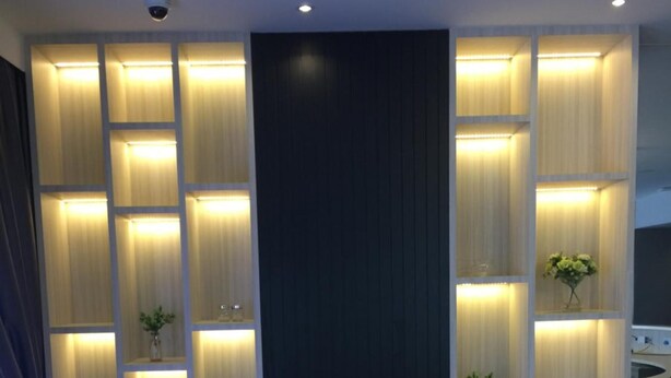 A modern reception area with a curved reception desk, illuminated shelving units, and a dark accent wall. - JB Central Hotel (Johor Bahru)