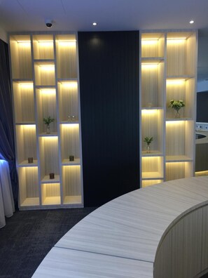 A modern reception area with a curved reception desk, illuminated shelving units, and a dark accent wall. - JB Central Hotel (Johor Bahru)