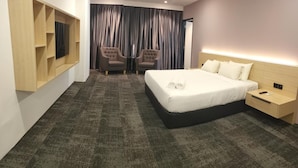 A modern hotel room with a large bed, a TV mounted on the wall, two armchairs, and a nightstand with a remote control. - JB Central Hotel (Johor Bahru)