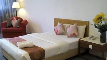 A hotel room with a bed, a chair, a nightstand, and a lamp.