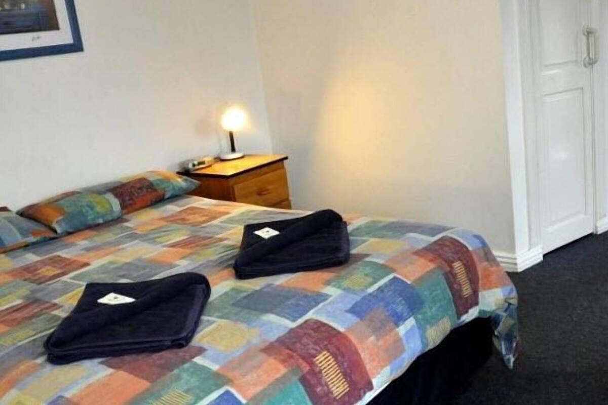 A hotel room with a bed, a nightstand, a lamp, and a door.