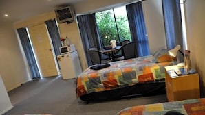 Habitación de hotel con cama, escritorio, silla, televisor y ventana con cortinas.