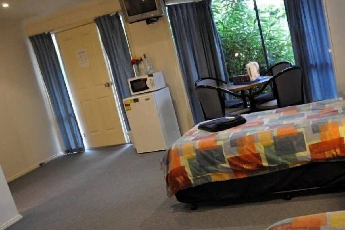 A hotel room with a bed, a desk, a chair, a microwave, and a view of greenery outside.