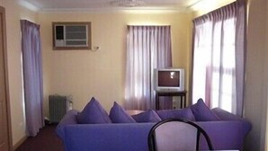 Una habitación con un sofá morado, una mesita pequeña y un televisor sobre un mueble.