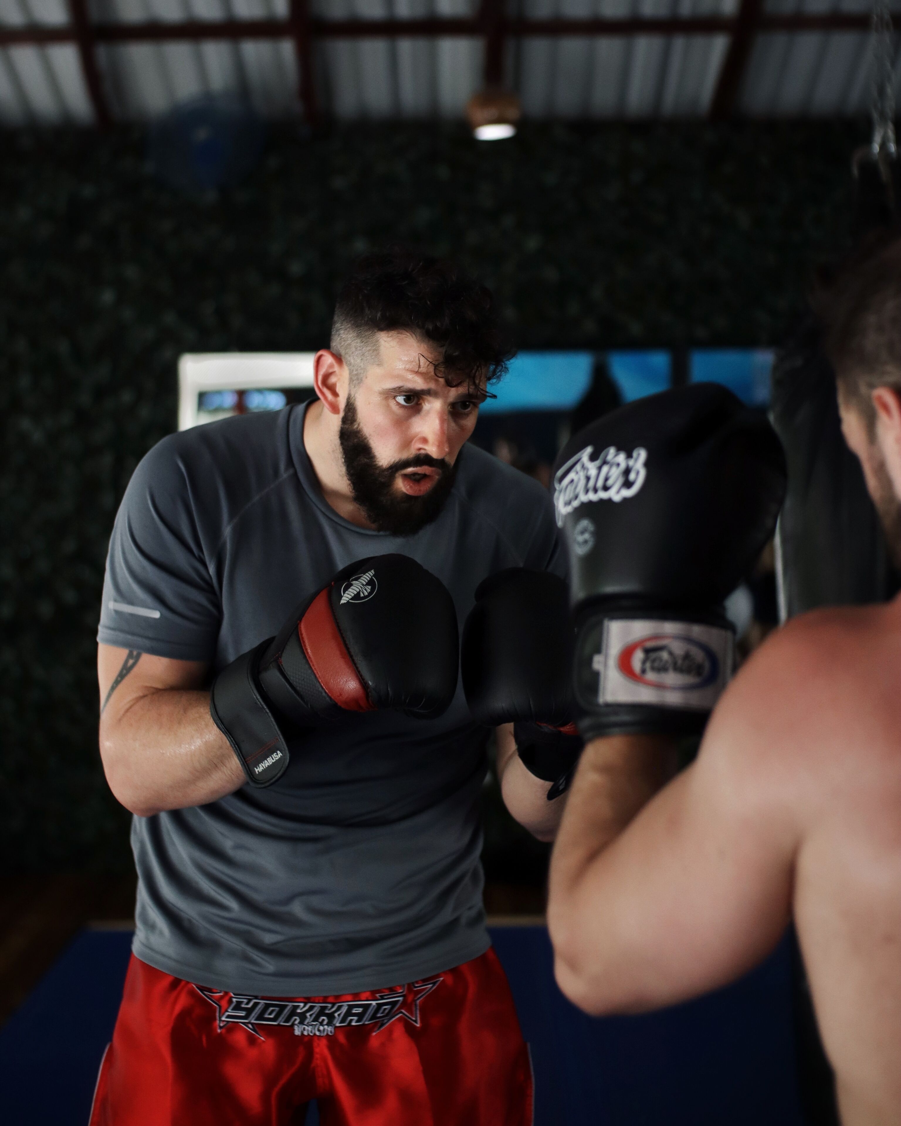 A person in a grey t-shirt and red shorts practicing boxing with a punching bag.