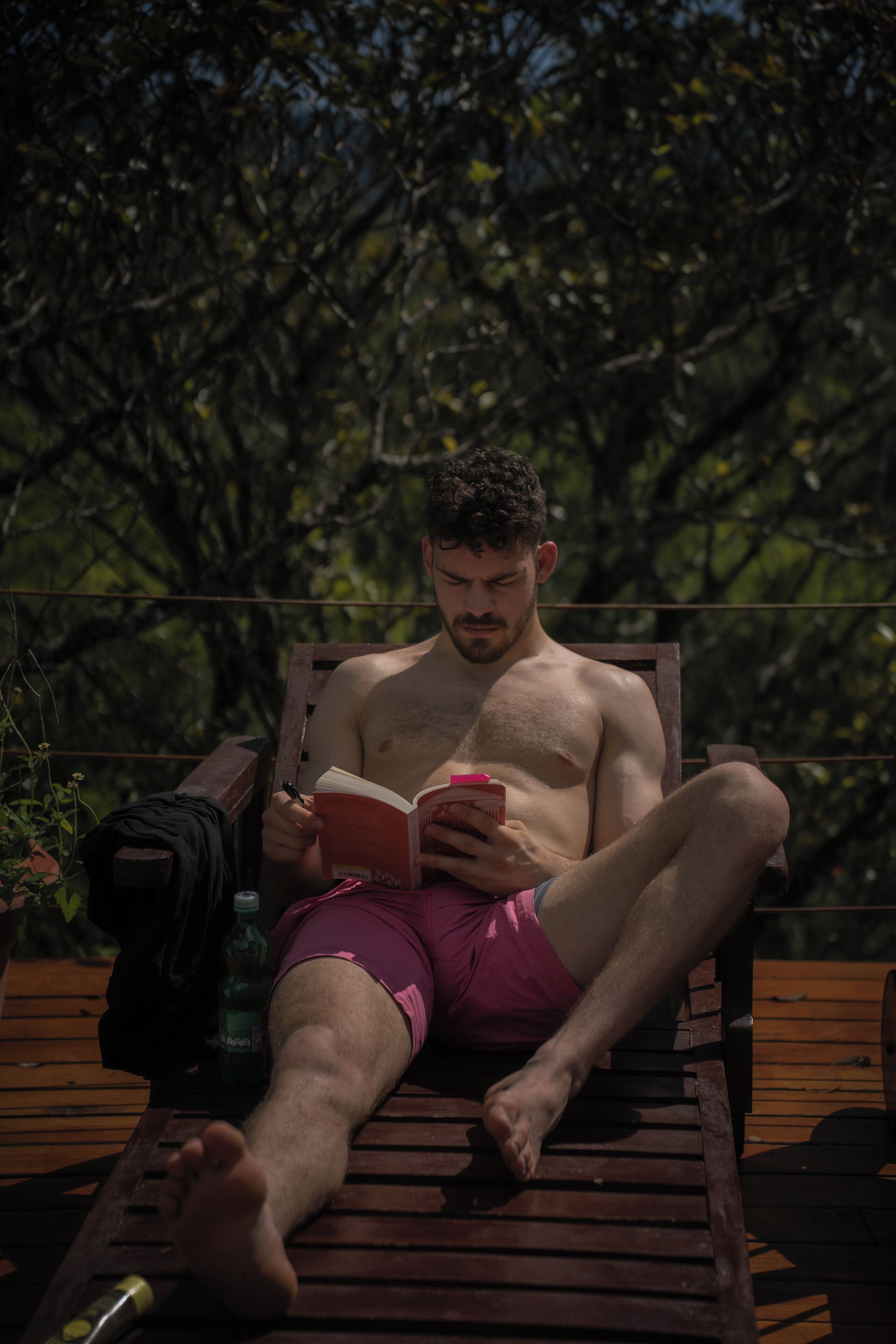 A person sitting on a wooden deck chair reading a book.