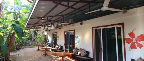 A covered outdoor seating area with tables and benches, surrounded by vegetation.