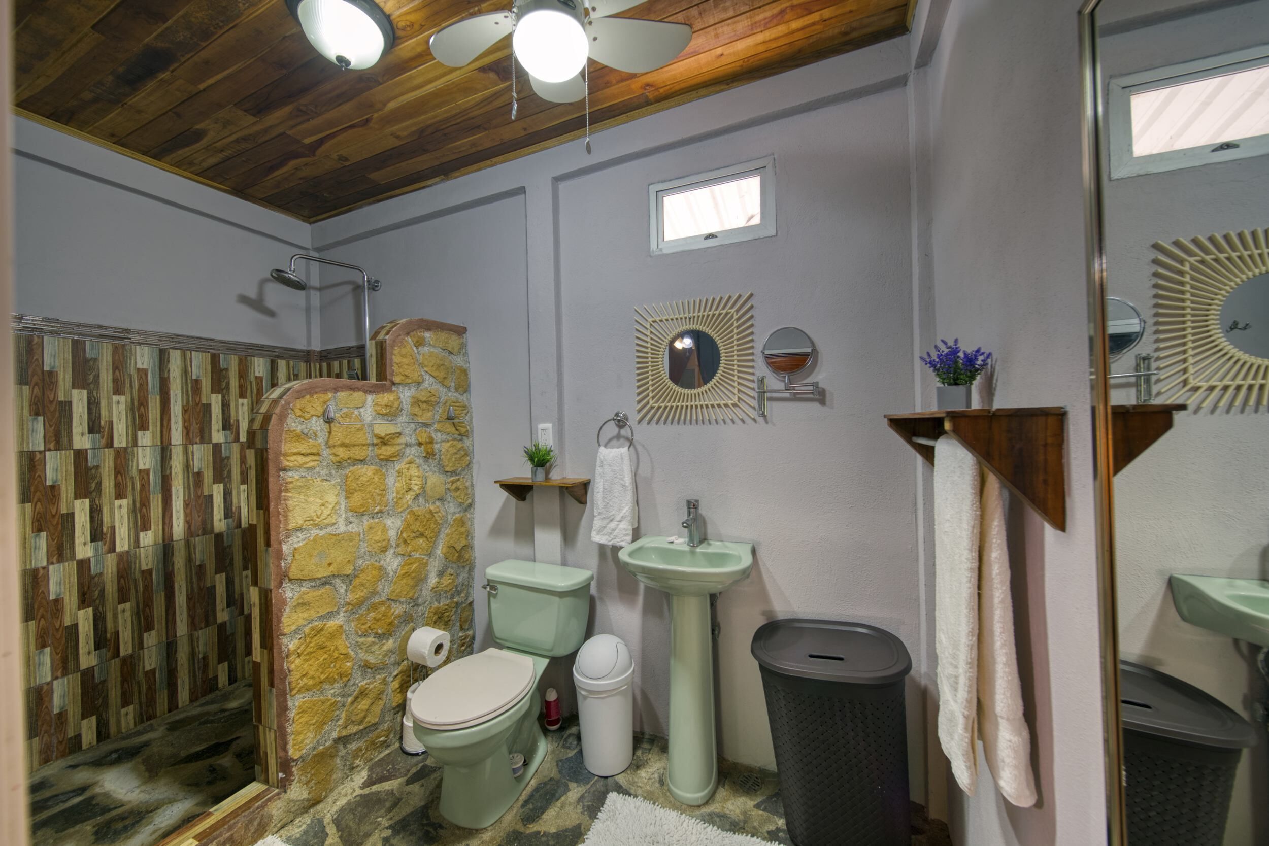 A bathroom with a stone shower enclosure, a toilet, a sink, and a trash bin.