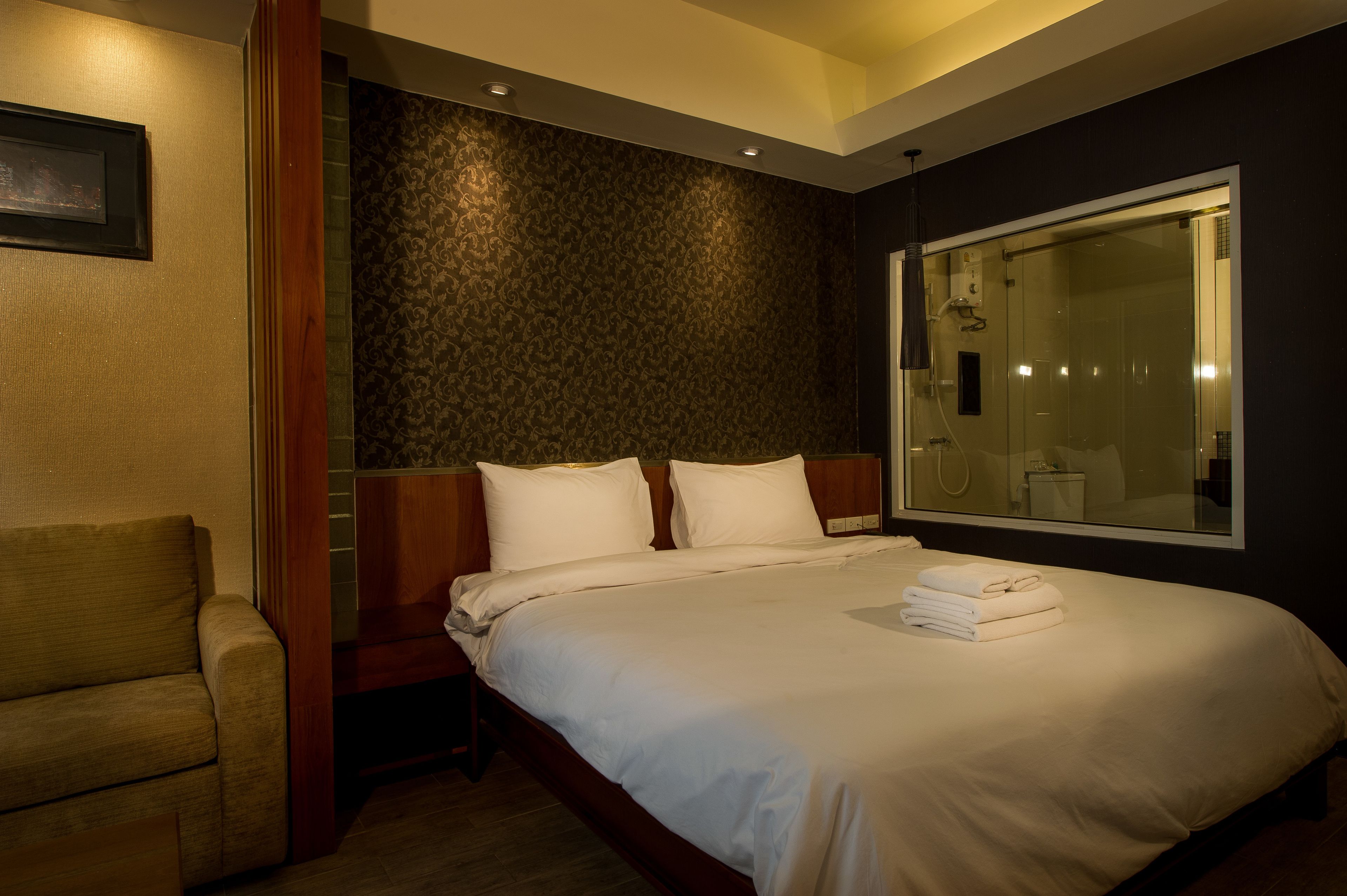 Une chambre d’hôtel avec un grand lit, une tête de lit en bois, un mur à motifs sombres et une grande fenêtre.