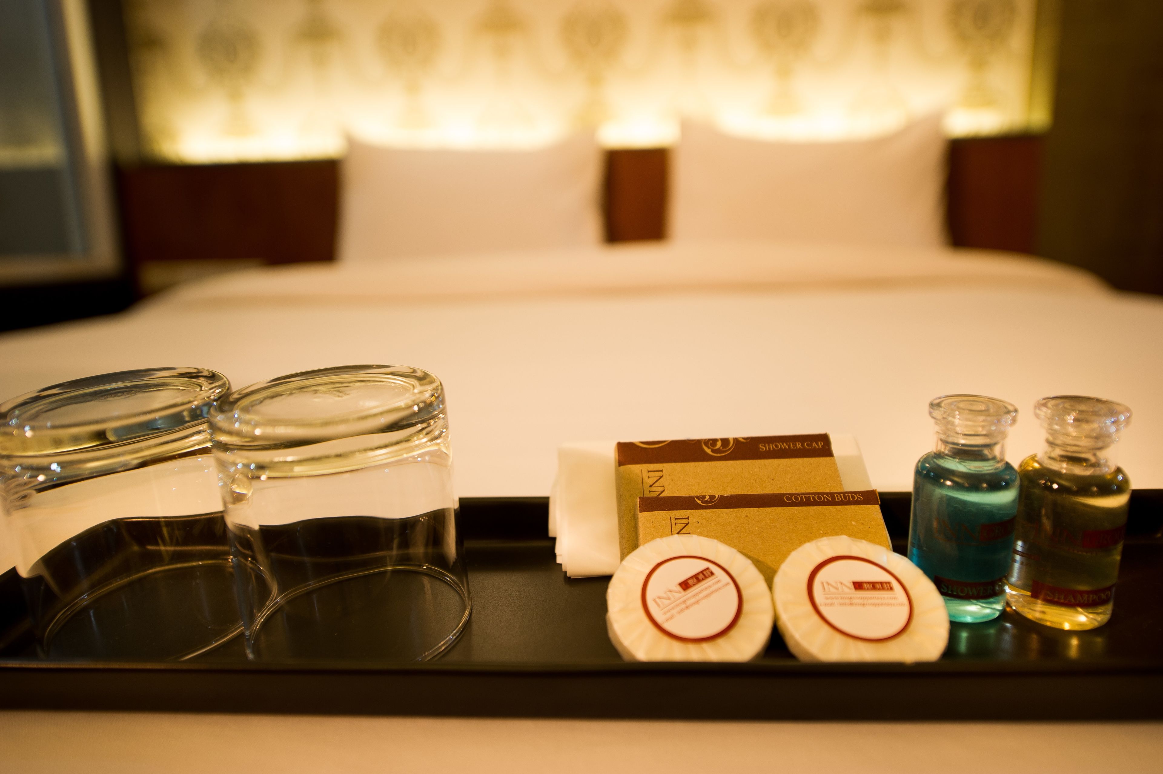 A hotel room with a neatly made bed, a tray with toiletries including a shower cap, cotton buds, and two bottles of shampoo.