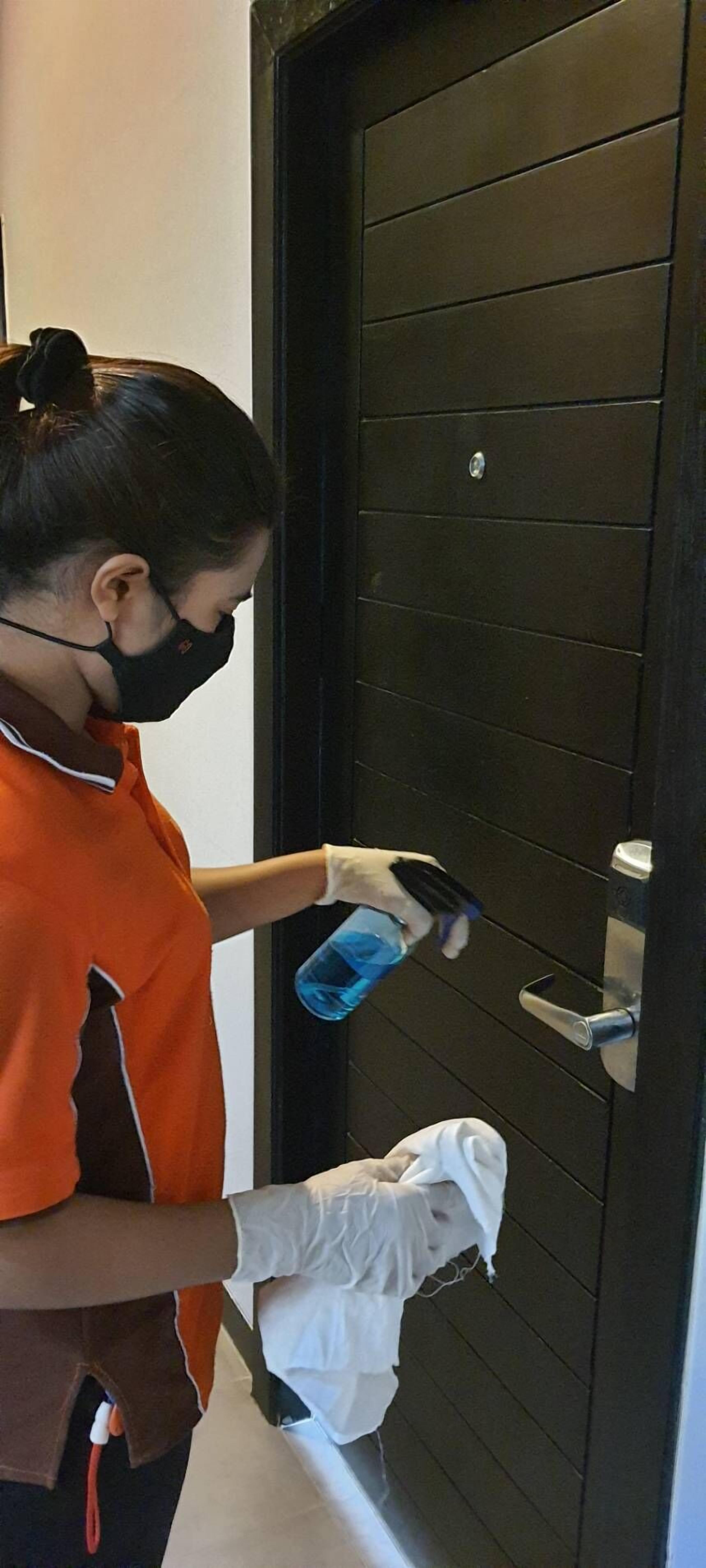 A person cleaning a door handle with a cloth and a spray bottle.