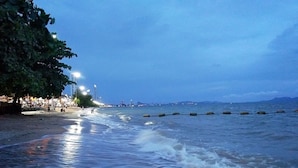 Une plage aux eaux calmes, une promenade bordée d’arbres et les lumières lointaines de la ville.