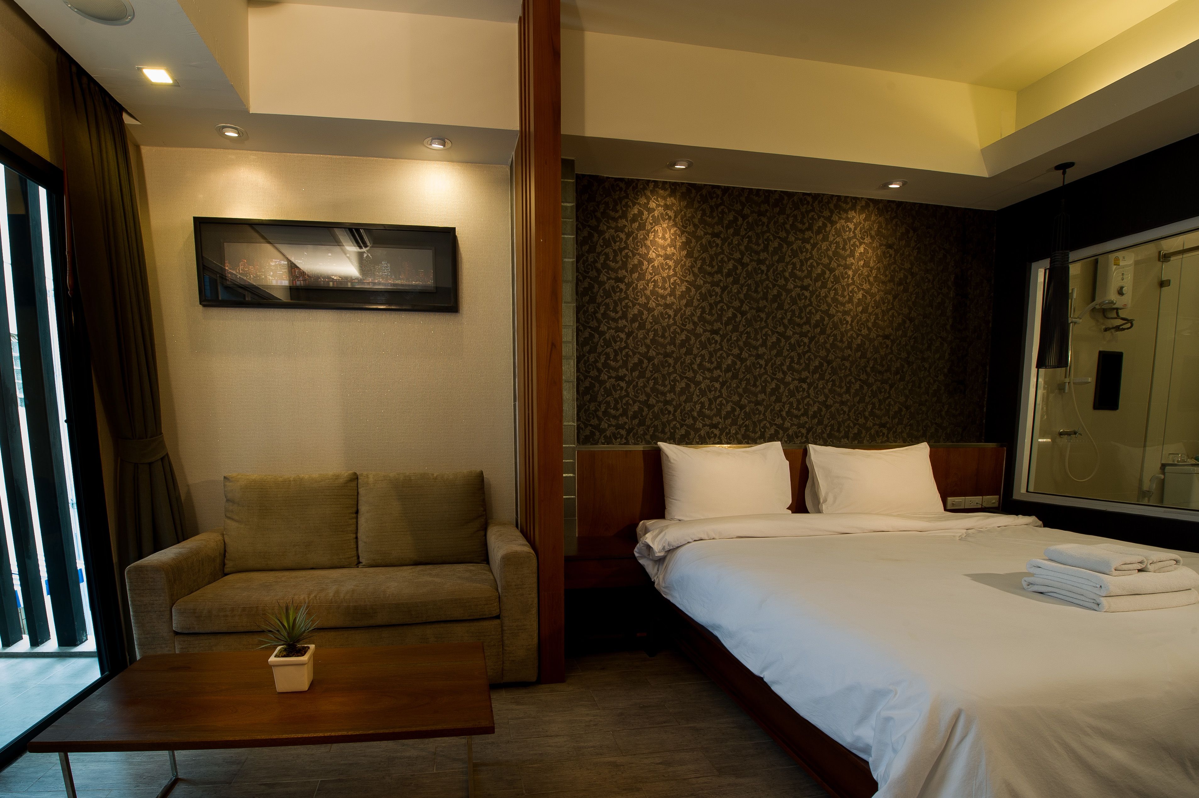 A hotel room with a bed, a sofa, a small table with a plant, and a large mirror.