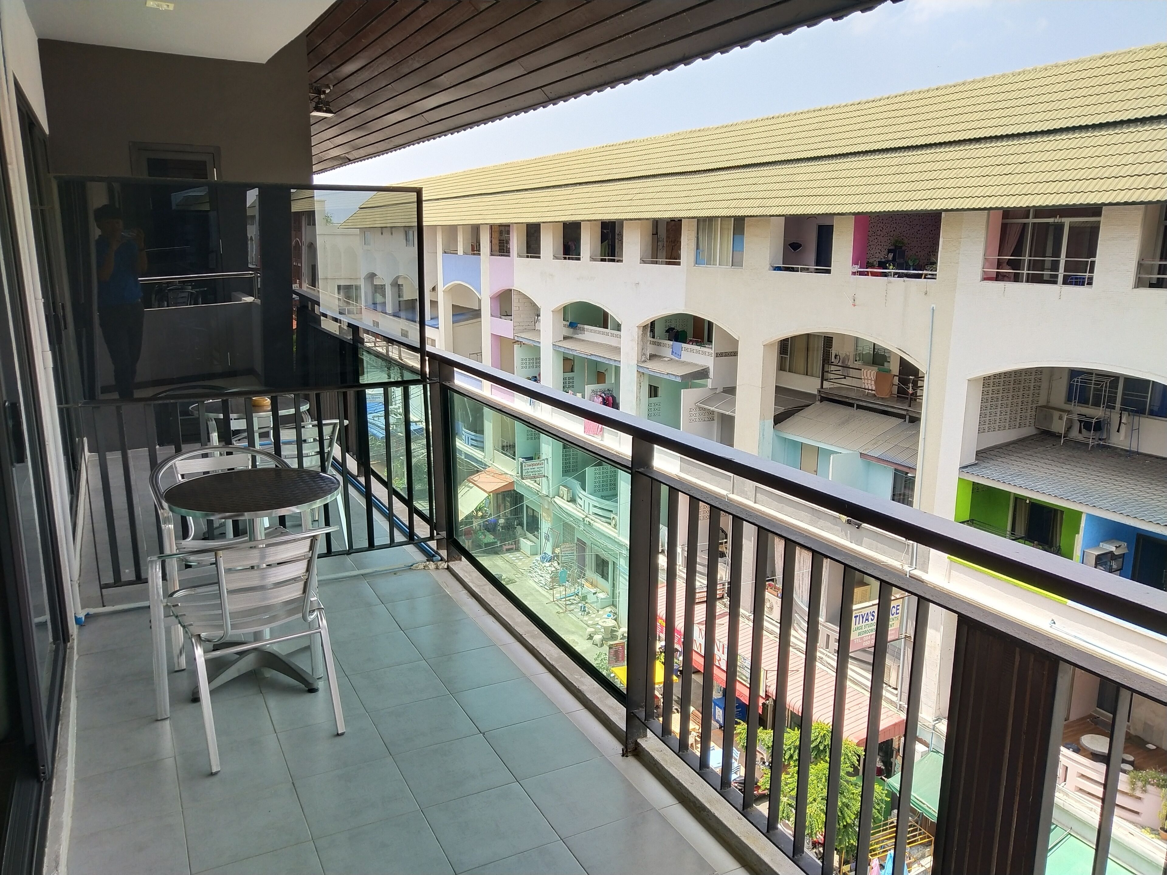 A balcony with a table and chair, overlooking a multi-story building with balconies.