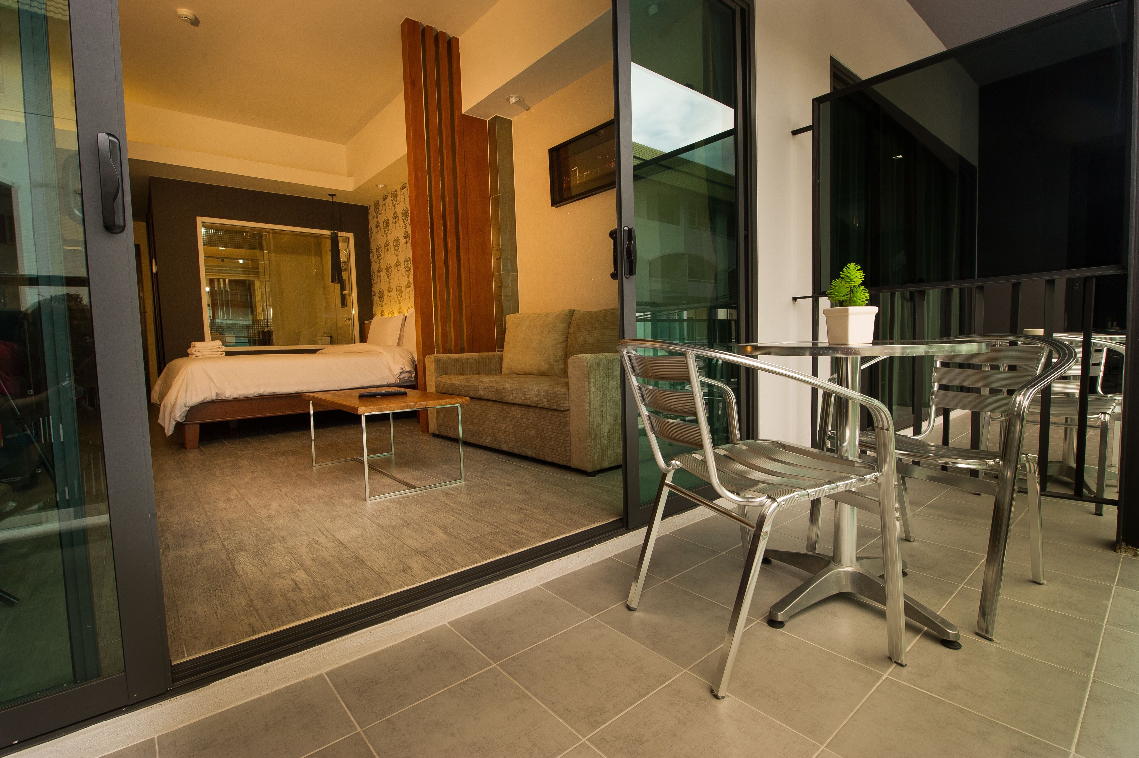 Ein modernes Hotelzimmer mit einem Bett, einem Sofa, einer Glastür zu einem Balkon und einem Essbereich mit Stühlen und einem Tisch.